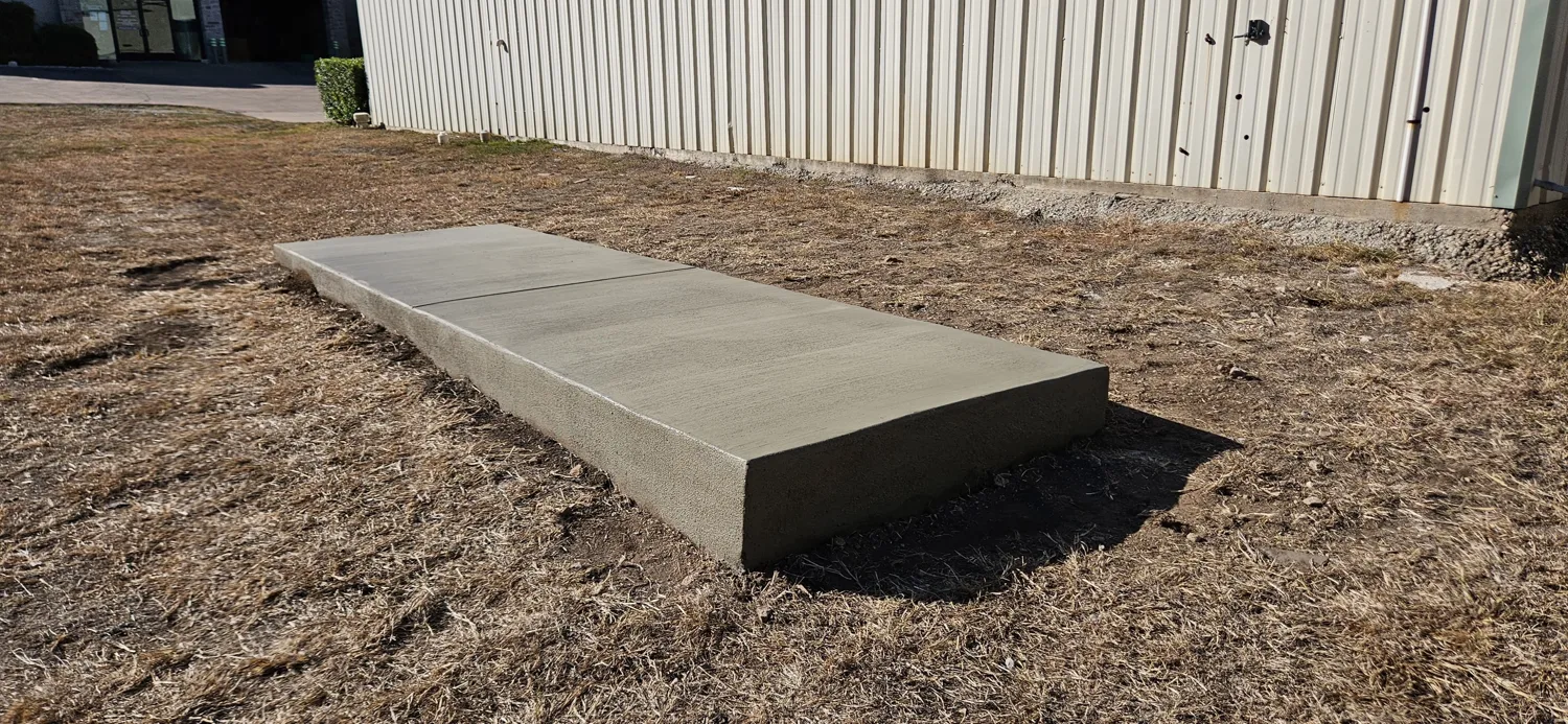 Finished reinforced concrete equipment pad poured beside a metal building